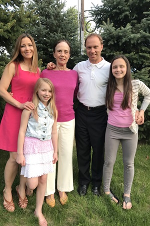 Family consisting of a young woman, two little girls, mother and father all stand outside wearing pink and white for mother's day